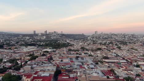 Volando-Sobre-Casas-Residenciales-Desde-El-Mirador-De-Los-Arcos-Al-Atardecer-En-Querétaro,-México