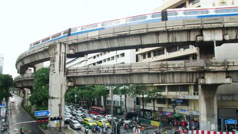BTS-Sky-Train-on-rail-tracks-over-traffic-through-busy-intersections-at-rush-hour-in-Bangkok-which-is-controlled-by-traffic-lights,-there-is-heavy-traffic-every-day