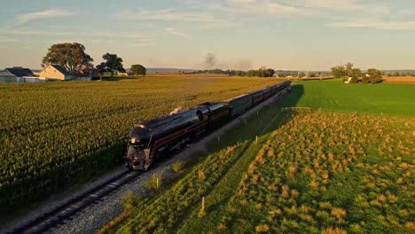 An-Aerial-View-on-a-Steam-Engine-and-Passenger-Coaches-Approaching-Blowing-Smoke-and-Steam-Following-Train-From-in-Front-and-to-the-Side-During-the-Golden-Hour