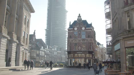 Tilt-up-from-busy-city-square-to-distant-Dom-tower-under-renovation-in-Utrecht-city,-the-Netherlands