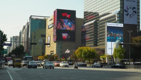 Los-Autos-Comienzan-A-Moverse-En-El-Semáforo-Verde-En-La-Carretera-Teheran-ro-En-Seúl-Cerca-Del-Gran-Hotel-Intercontinental-Coex,-Los-Grandes-Almacenes-Hyundai,-La-Estación-Samseong-En-Otoño,-Enormes-Vallas-Publicitarias-Al-Aire-Libre