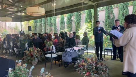 Choir-singing-melodies-for-a-wedding-in-a-decorated-glass-place-where-the-bride-and-groom-are-seated-in-the-background