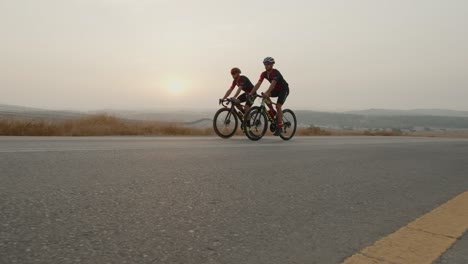 slow-motion-of-two-road-cycelist-professionals-riding-in-the-desert's-empty-lonely-road-at-sunrise