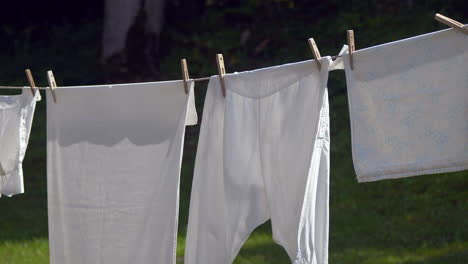 Panning-shot-of-white-laundry-drying-outdoors-on-clothesline-between-trees-in-garden-,close-up