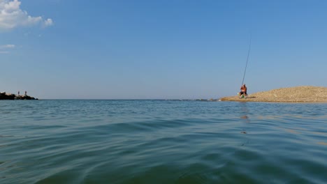 Low-angle-sea-level-pov-from-boat-sailing-forward-to-mouth-of-Sinello-river-in-Abruzzo-with-fisherman-catching-fish-in-background,-Italy