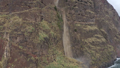 Beautiful-waterfall-rolling-across-the-stone-wall-in-the-mountains-in-Madeira,-Portugal---aerial-drone-shot