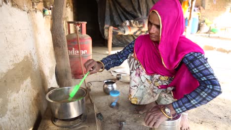 Poor-Indian-woman-preparing-tea-on-ground-with-pot-and-gas-stove-cooker-in-rural-village-of-Rajasthan-in-India