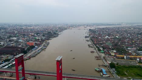 Red-color-bridge-pf-Ampera-over-Musi-river-with-cityscape-of-Palembang,-aerial-view