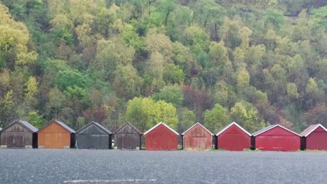 Row-Of-Traditional-Norwegian-Rorbuer-Cabins-In-The-Rain-With-Autumnal-Trees-In-Background