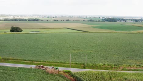 Farmer-on-John-Deere-put-put-Model-A-tractor-pulls-wagon-of-logs-on-road-through-rural-farmland-in-America