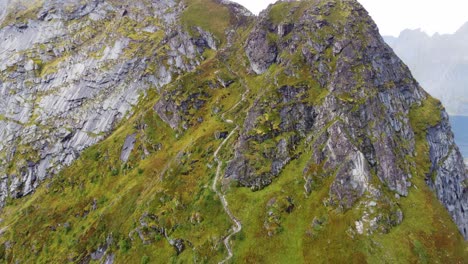 Path-to-steep-mountain-surrounded-by-the-sea-in-northern-Norway-with-people-climbing-up-stairs-to-the-top-filmed-by-drone