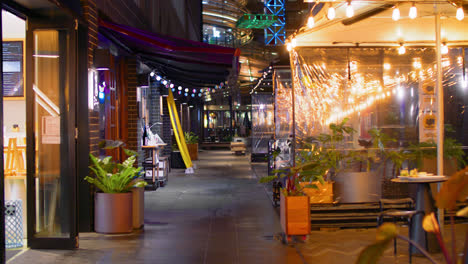 Personas-Enmascaradas-Caminando-En-La-Calle-Con-Restaurantes-Vacíos-Al-Aire-Libre-Por-La-Noche-Durante-El-Cierre-De-Covid-19-En-Sydney,-Nsw,-Australia