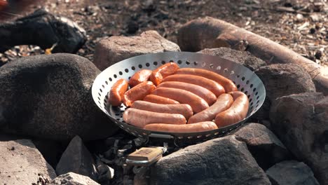 A-man-puts-grilled-sausages-in-a-pan-on-a-campfire