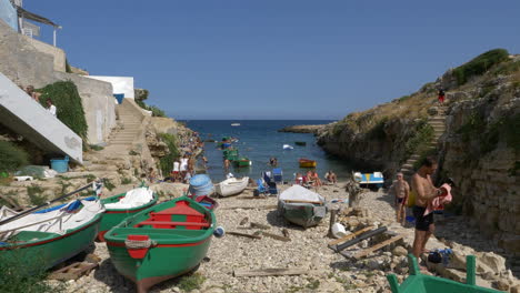 Boats-And-People-On-The-Stony-Shore-At-The-Beach-In-Port-Alga,-Polignano-a-Mare,-Apulia,-Italy