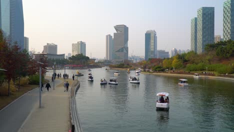 Leisure-activities-in-Songdo-Central-Park-at-sunset-with-view-on-G-Tower---people-enjoying-walking-by-the-lake-and-travel-by-boats-in-autumn
