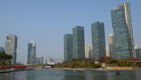 Schützen-Sie-Eine-Person,-Die-Wasserski-Auf-Einem-See-Im-Songdo-Central-Park-Mit-Modernen-Futuristischen-Wolkenkratzern-Und-Der-Städtischen-Skyline-Von-Incheon-Im-Herbst-Fährt-–-Weitwinkelaufnahme