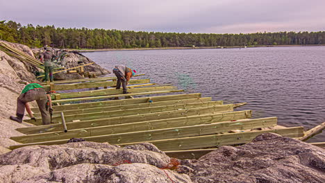workers-build-a-wooden-deck-structure-on-lakeside-rock