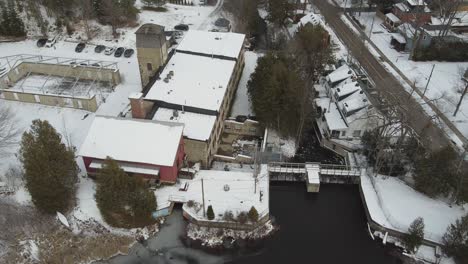 Aerial-Shot-Of-Historic-Alton-Mill-During-Winter,-Water-From-Pond-Flowing-Over-Waterfall