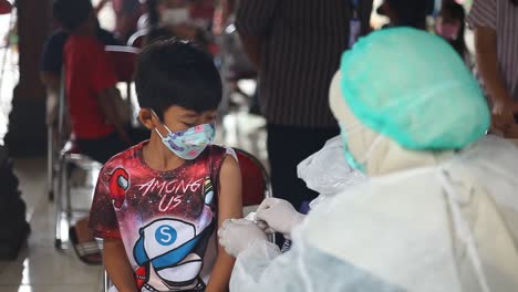 Yogyakarta,-Indonesia---Dec-20,-2021-:-an-elementary-school-boy-is-receiving-a-covid-19-vaccine-while-showing-a-thumbs-up