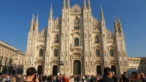 Tilt-down-of-tourist-taking-photo-with-smartphone-at-friends-posing-in-Duomo-di-Milano-or-Milan-Cathedral-square-in-Italy
