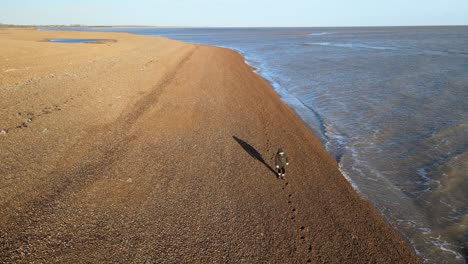 Drone-tracking-Lone-Female-walking-along-shingle-beach-in-Suffolk-bright-sunny-day