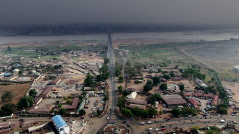Highway,-roundabout-and-bridge-with-the-Benue-River-and-densely-populated-city-on-the-horizon-in-Nigeria,-West-Africa---aerial-view