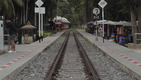 A-static-shot-from-the-middle-of-the-railway-track-and-platform-of-Kwai-Bridge-Station,-an-iconic-landmark-built-during-World-War-2-and-a-popular-tourist-destination-in-Kanchanaburi,-Thailand