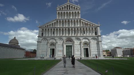 View-a-couple-walking-in-front-of-the-Pisa-Cathedral-in-Piazza-dei-Miracoli-in-Miracle-Square-in-Italy-with-close-view-of-the-beautiful-paintings-on-the-outer-wall-of-the-Cathedral