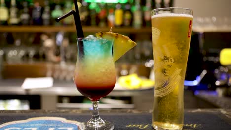 Zeitlupe-Eines-Glases-Kaltes-Bier-Und-Eines-Cocktails-Auf-Dem-Bargelände-In-Einem-Nachtclub