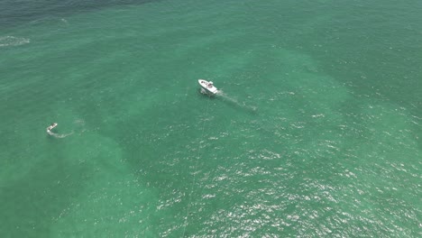 Aerial-flies-over-multicolor-parasail-and-boat-in-shallow-green-water