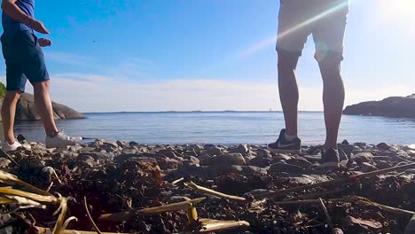 Couple-of-guys-throwing-rocks-on-rocky-Scandinavian-beach,-back-slow-motion-shot-of-stone-skipping