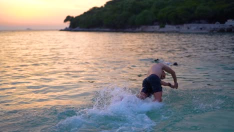 Young-male-joyfully-diving-into-the-ocean-on-a-beautiful-tropical-island-at-sunset