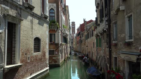 Venice-narrow-Canal-view-of-a-romantic-gondola-and-old-church-bell-tower-in-the-background-revealing-skyline-of-old-city-center