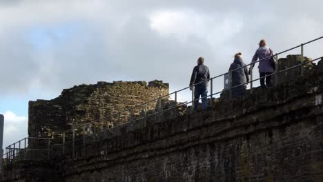 Tourists-walking-along-Conwy-castle-ruins-battlements-overlooking-Welsh-town-at-sunrise