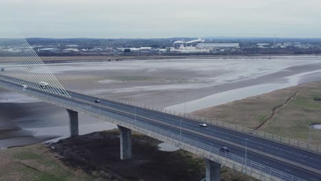 Aerial-view-Mersey-Gateway-cable-stayed-toll-bridge-traffic-crossing-River-Mersey-at-low-tide-zoom-in-to-highway