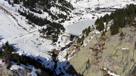 Aerial:-flying-over-a-viewpoint,-a-dam-with-some-people-and-a-frozen-lake