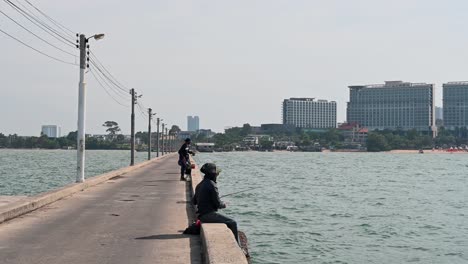 A-man-sitting-reeling-in-the-lure-at-the-Pattaya-Fishing-Dock,-Chonburi,-Thailand