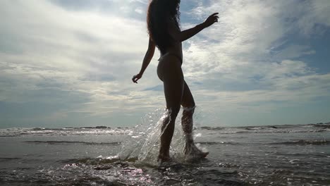 Beautiful-young-woman-walks-on-beach-and-splashes-in-sea-on-holiday