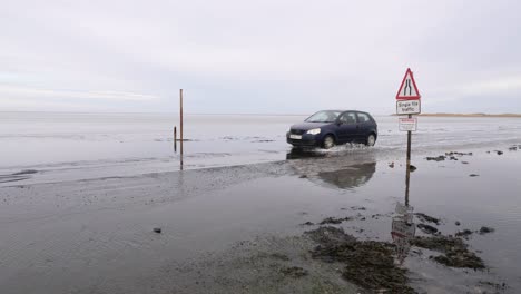 Car-driving-along-low-flooded-road-past-warning-sign