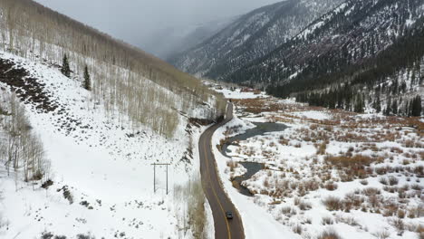 Car-driving-on-mountain-side-road-during-winter-season,-high-angle-drone-view
