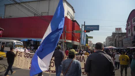 Manifestante-Camina-Entre-La-Multitud-Portando-La-Bandera-Nacional-Durante-Una-Marcha-Pacífica-En-Las-Calles-De-La-Ciudad-Contra-El-Actual-Presidente-Nayib-Bukele---Cámara-Lenta