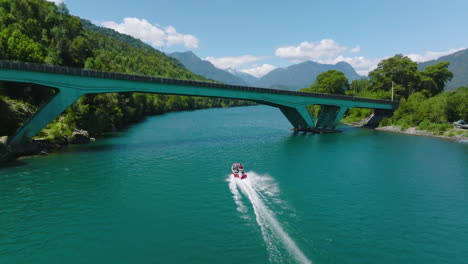 Aerial-Following-Speed-Boat-Along-Puelo-River-Going-Under-Low-Bridge-In-Chile,-Lake-District