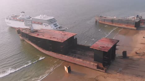 Aerial-View-Of-Half-Rusty-Ships-Hull-On-Beach-At-Gadani-With-White-Cruise-Liner-In-Between