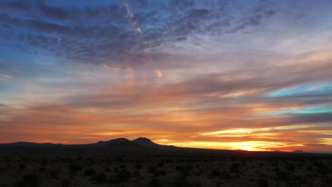 A-golden-dawn-over-the-Mojave-Desert-with-distant-mountains-in-silhouette-against-the-colors-of-the-sky-at-sunrise---aerial-pull-back-view