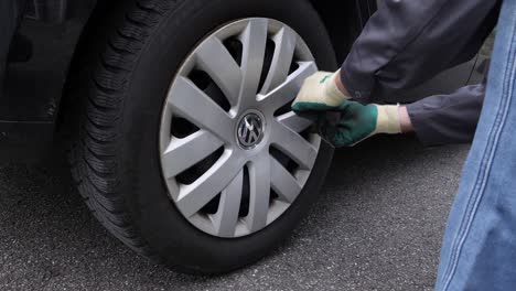 DIY-man-removes-hubcap-cover-with-gloves-to-change-tires,-closeup