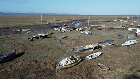 Various-stranded-abandoned-fishing-boat-wreck-shipyard-in-marsh-mud-low-tide-coastline-aerial-low-dolly-right-view