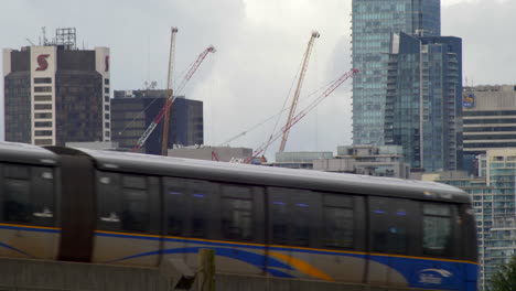 Passing-Canadian-train-and-construction-site-with-cranes-in-financial-district-of-Vancouver-in-Canada-during-cloudy-day