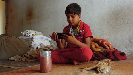 Der-Junge-Indische-Junge-Sitzt-Auf-Dem-Boden-Und-Schaut-Sich-Aufmerksam-Streaming-Videos-Auf-Dem-Smartphone-An
