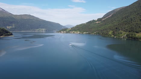 Entferntes-Boot-Verlässt-Den-Yachthafen-Und-Fährt-Aus-Dem-Lofjord-Gegen-Den-Innvikfjord-In-Lön,-Norwegen---Sonniger-Tag,-Vorwärts-Bewegte-Luftaufnahme