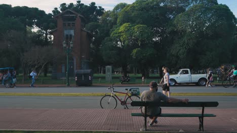 Ciclista-Se-Sienta-En-Un-Banco-Viendo-Pasar-A-La-Gente